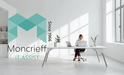 Moncrieff IT Assist branding displayed over a modern office workspace with a person using a laptop at a large desk in a bright, minimalist office environment.
